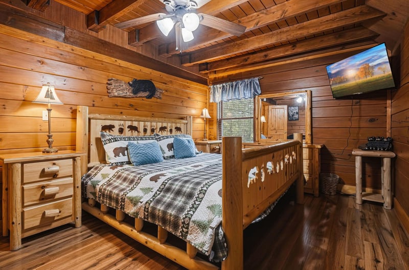 Unwind in this cozy rustic bedroom with exposed wood beams, warm pine walls, and a handcrafted log bed dressed in plaid and bearthemed linens. Natural light from the window and soft lamplight create 