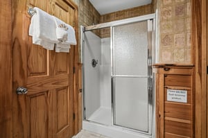 Step into your private bathroom featuring a spacious glassdoor shower, warm wood cabinetry, and fresh towels waiting for your arrival.