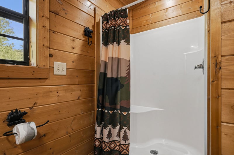 Step into your rustic cabin bathroom where warm wood walls and a geometric patterned curtain create cozy mountain vibes.