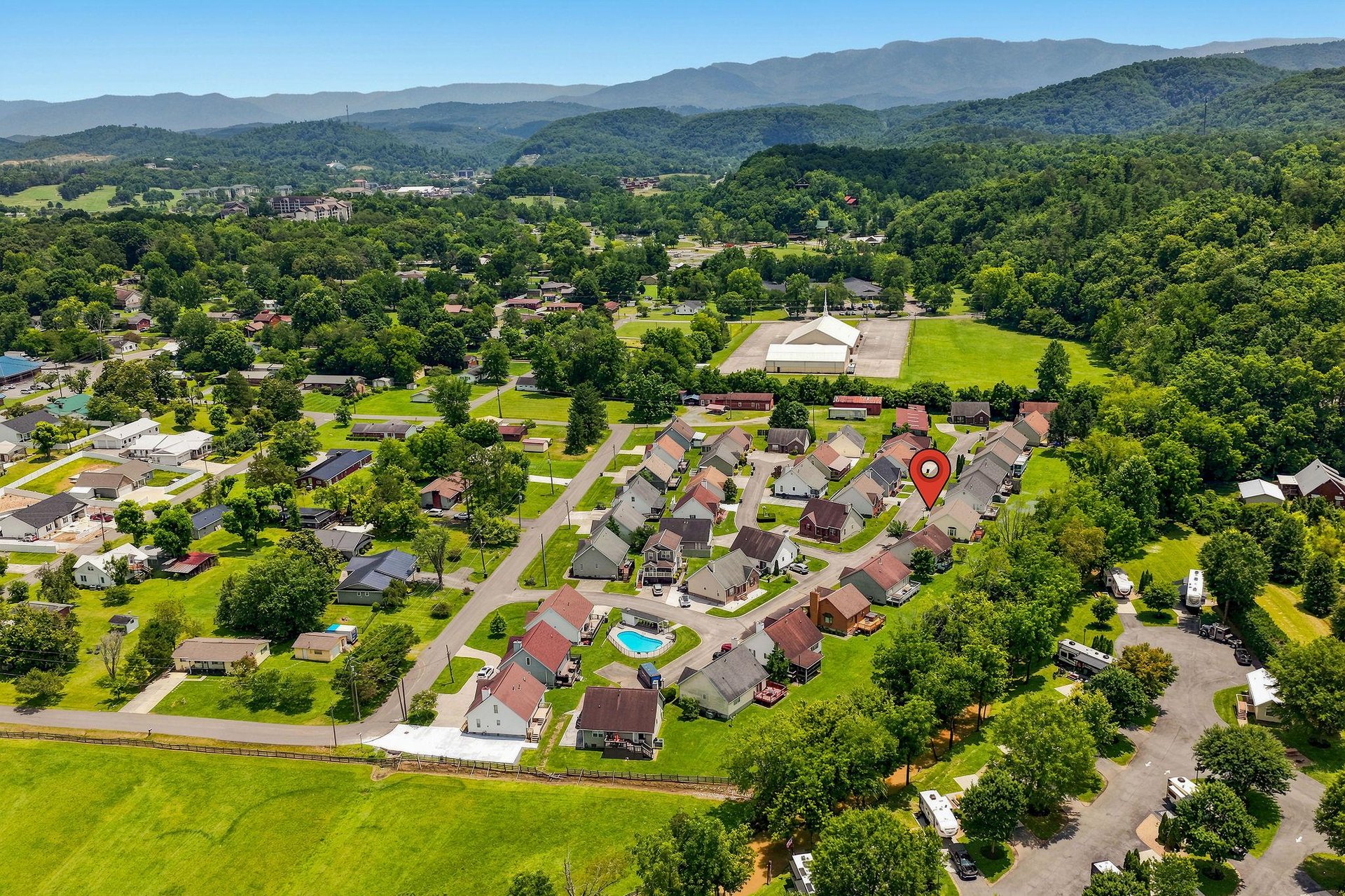Aerial view of a residential community nestled in a lush valley, surrounded by rolling mountains and abundant greenery, marking the location of this peaceful vacation rental property.