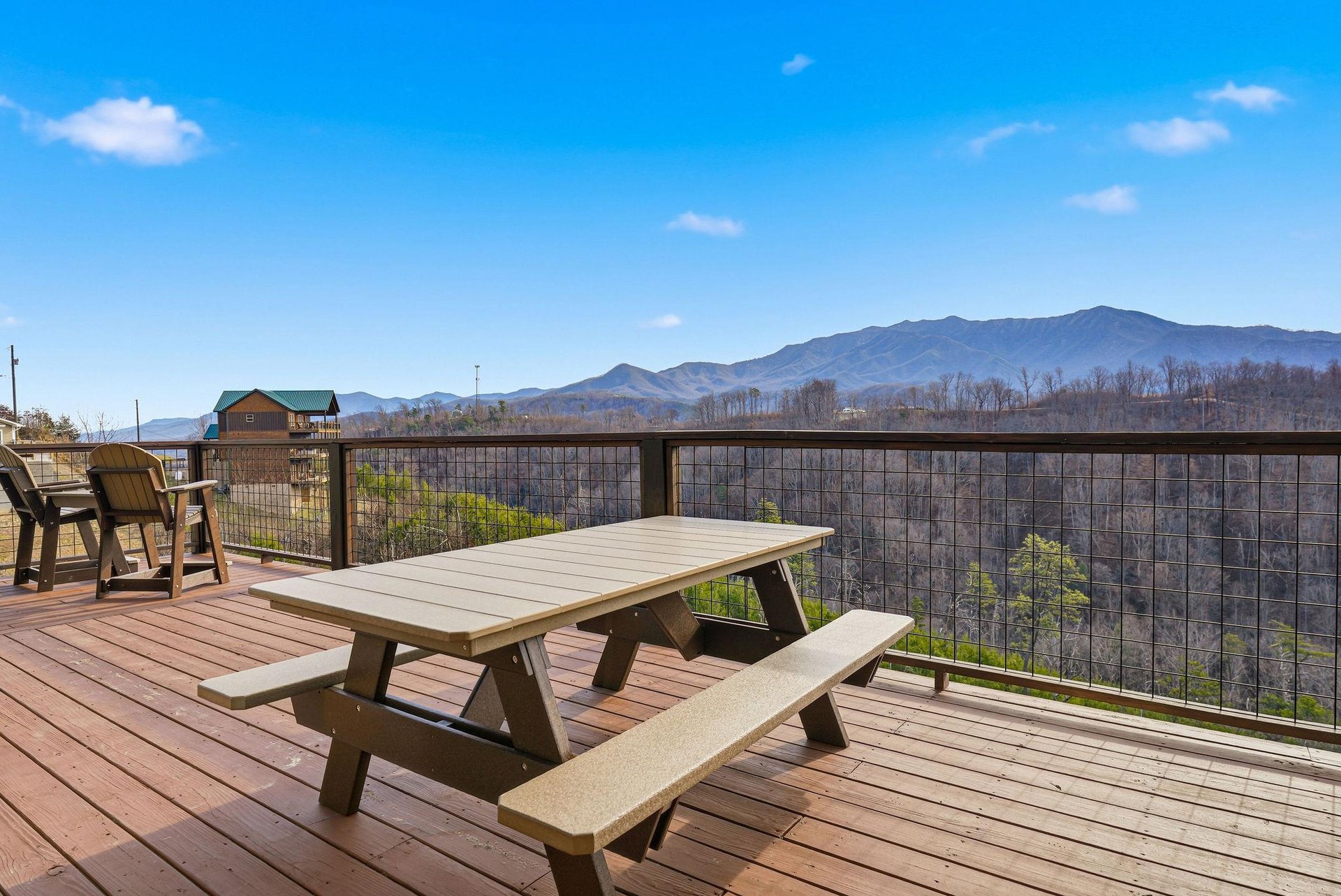 Spacious deck with picnic table overlooking stunning mountain ranges and forested valleys under clear blue skies.