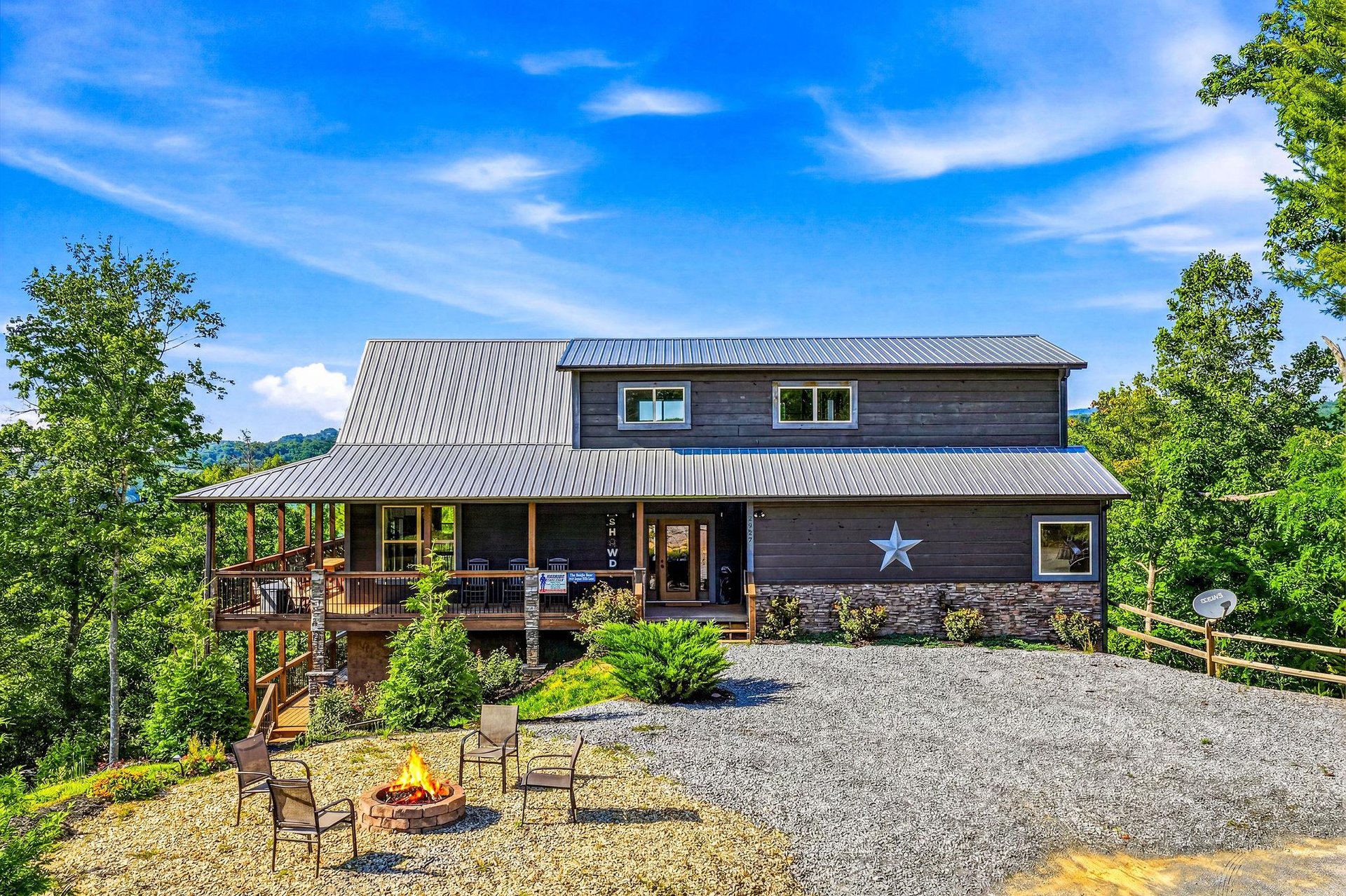A charming mountain retreat with a distinctive star marking the entrance, set among lush greenery and featuring a spacious fire pit area for evening gatherings.