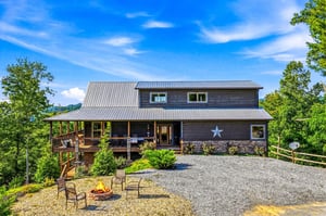 A charming mountain retreat with a distinctive star marking the entrance, set among lush greenery and featuring a spacious fire pit area for evening gatherings.