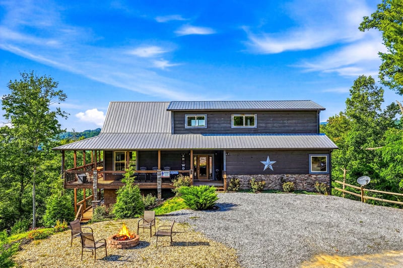 A charming mountain retreat with a distinctive star marking the entrance, set among lush greenery and featuring a spacious fire pit area for evening gatherings.
