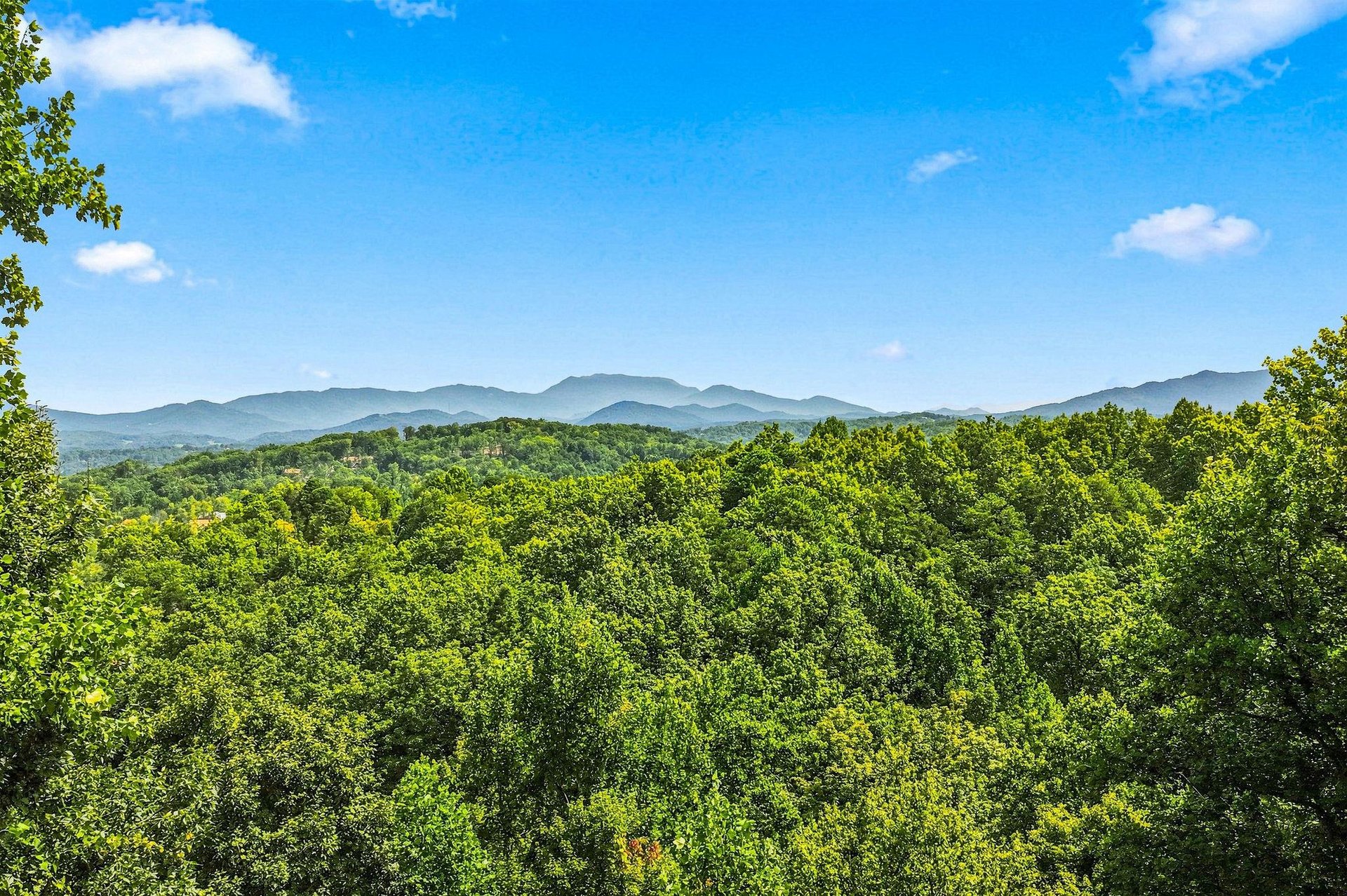 Stunning mountain ridges rise above lush green forests under a bright blue sky—a serene backdrop to the propertys natural surroundings.