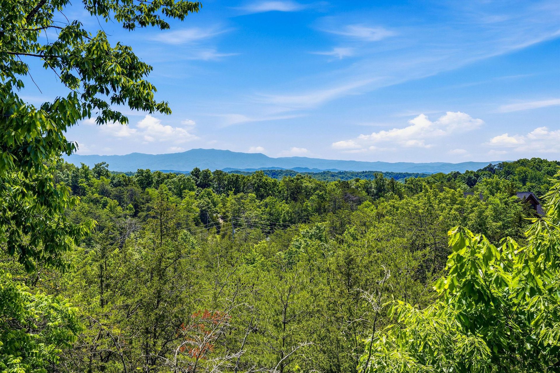 A scenic mountain vista framed by lush forested hills under bright blue skies, showcasing the propertys peaceful natural surroundings.