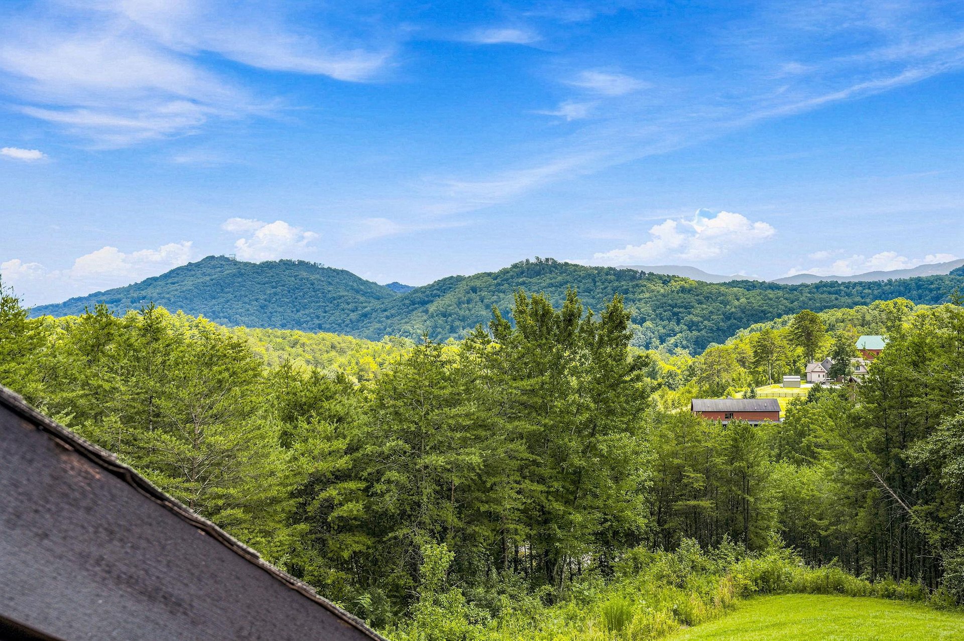 Expansive mountain vistas stretch across lush green valleys, offering a serene backdrop of rolling peaks and vibrant summer foliage under a bright blue sky.