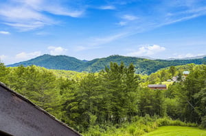 Expansive mountain vistas stretch across lush green valleys, offering a serene backdrop of rolling peaks and vibrant summer foliage under a bright blue sky.