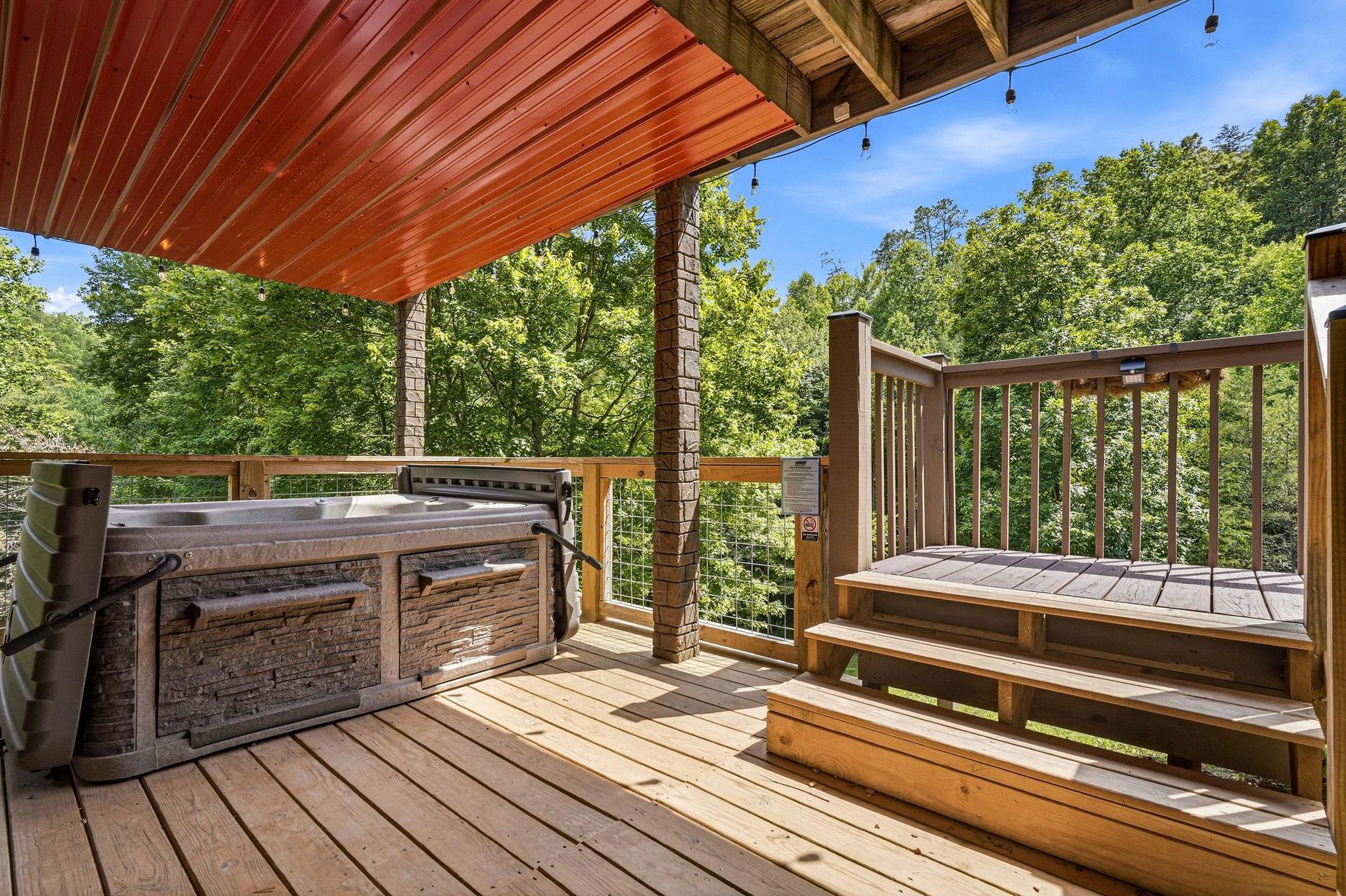 Unwind in your private hot tub under a covered deck, surrounded by lush forest views and bright blue skies—a perfect spot to relax and soak in natures beauty.