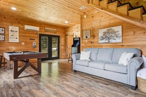 Step into your cabins spacious living area where warm wood walls meet modern comfort. Challenge friends to pool, unwind on the cozy sofa, or enjoy the vintage arcade—your perfect retreat awaits.