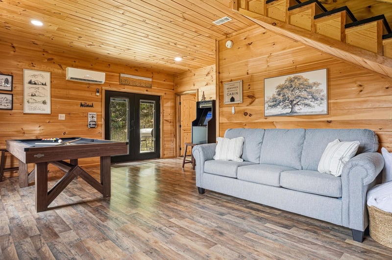 Step into your cabins spacious living area where warm wood walls meet modern comfort. Challenge friends to pool, unwind on the cozy sofa, or enjoy the vintage arcade—your perfect retreat awaits.