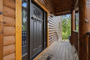 Charming log cabin entrance with rustic wood beams and a welcoming covered porch surrounded by natural greenery.