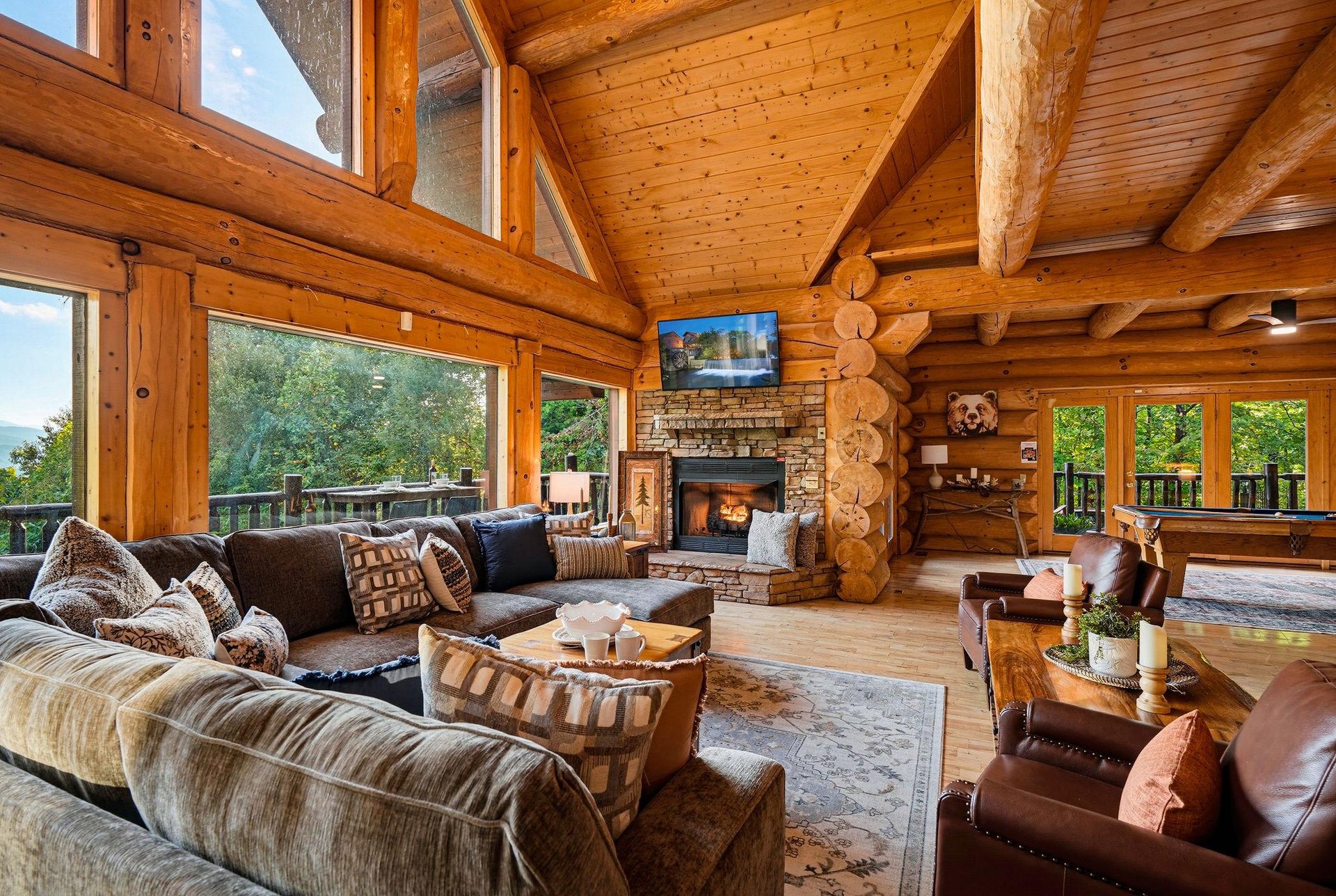 Step inside a stunning log cabin living room with soaring vaulted ceilings, handhewn beams, and warm natural wood throughout. Your cozy gathering space features plush seating, a stone fireplace, and 