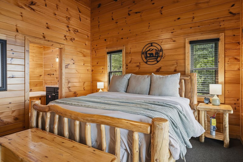 Sink into soft linens and rustic charm in your cozy bedroom, where warm wood surrounds you and natural light filters through the windows for your mountain retreat.