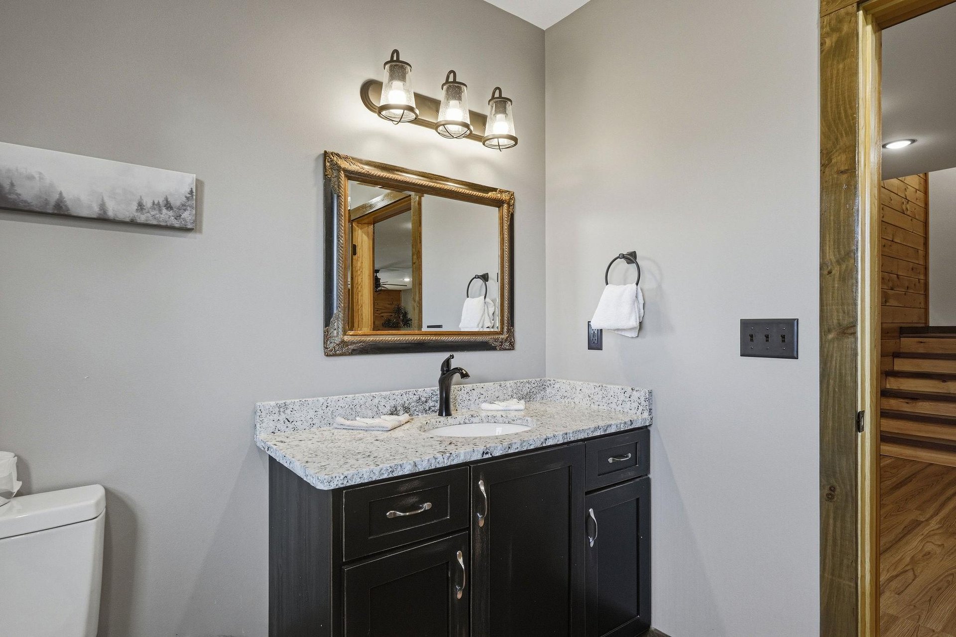 Your private bathroom features a stylish dark vanity with granite countertop, warm lighting, and fresh towels ready for you.
