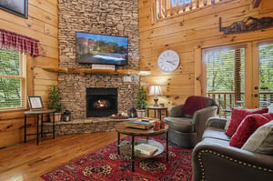 Cozy up in this warm living room with a stone fireplace, comfy seating, and natural light streaming through the windows. Perfect for your mountain retreat moments.