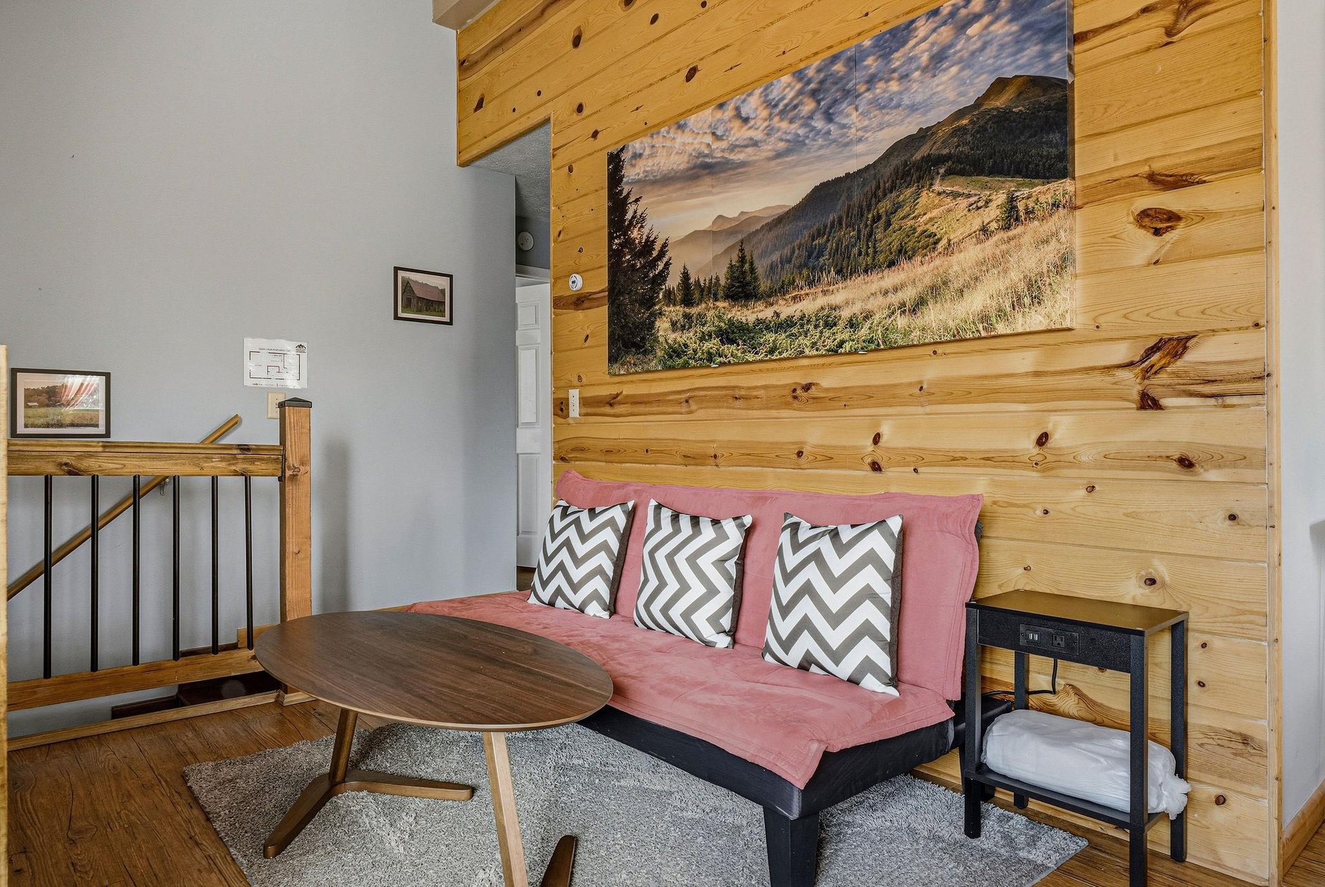 Unwind on your cozy pink sofa beneath stunning mountain artwork, where rustic wood beams meet modern comfort in your peaceful retreat.