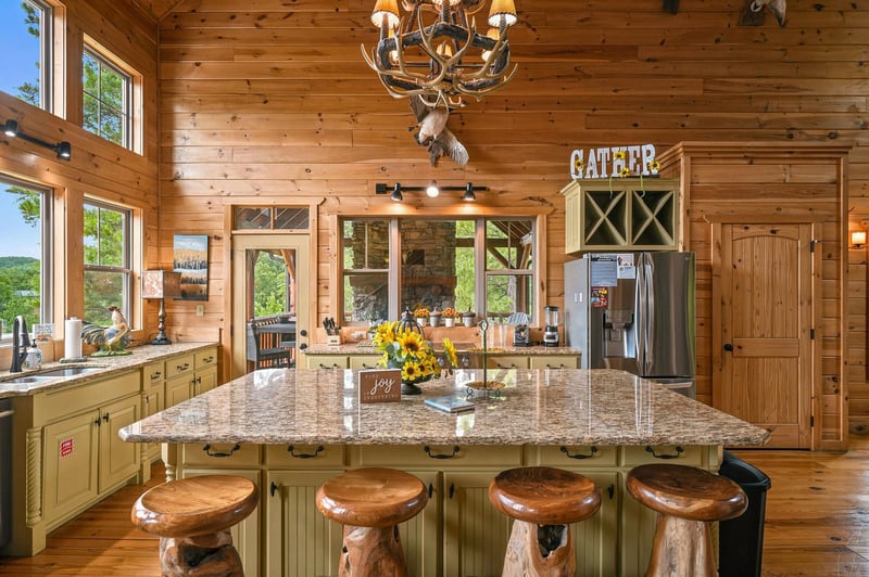 Gather around this stunning kitchen island with its gleaming granite countertop and rustic wood stools, where sunlight streams through soaring windows to brighten your mountain retreat.