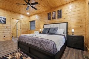 Rest peacefully in your rustic retreat featuring warm wood walls, plush bedding, and gentle ceiling fan breezes for the perfect mountain escape.