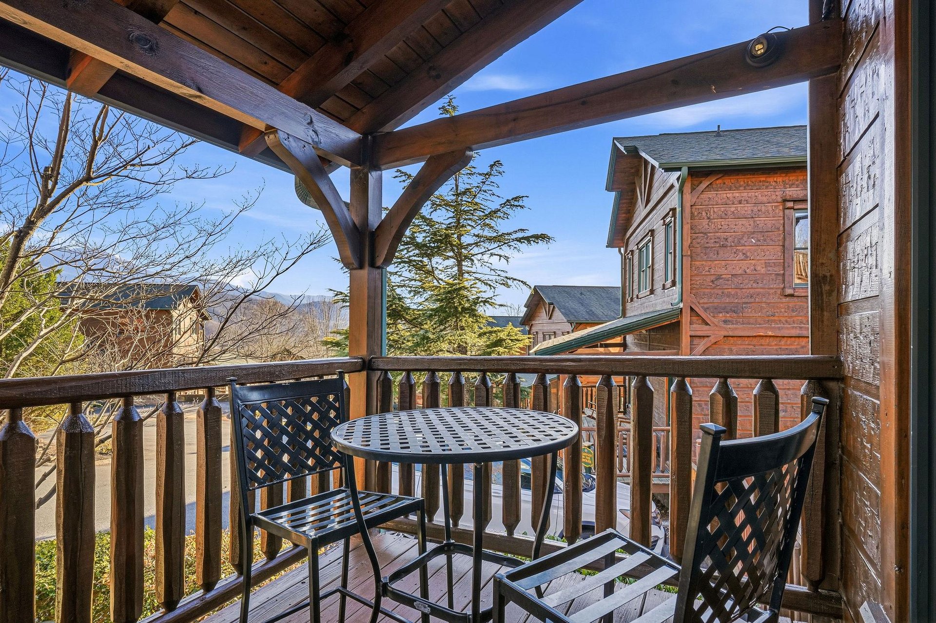 A covered balcony overlooks scenic mountain vistas and neighboring cabins, with a cozy bistro table inviting you to enjoy morning coffee or evening relaxation in the fresh air.