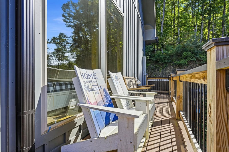 Step onto your private deck framed by lush forest views, where Adirondack chairs invite you to unwind in the fresh mountain air with a cozy throw and peaceful woodland scenery.