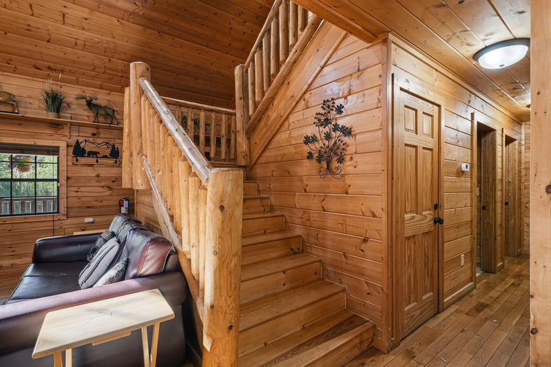 Step into your cozy log cabin where rustic charm surrounds you with warm wood walls, a comfortable leather sofa, and handcrafted staircase.
