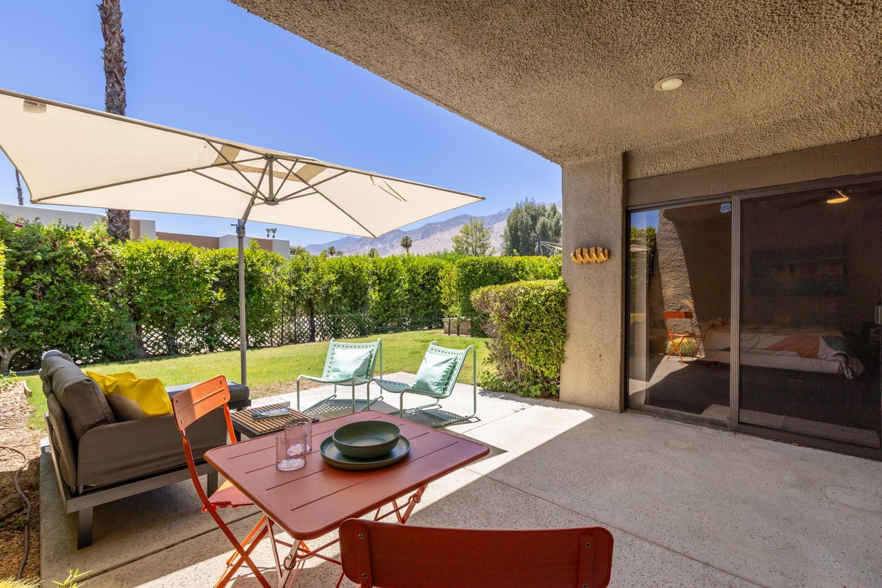 Back patio located off of the living room and primary bedroom featuring a table and chairs for morning coffee, umbrella, and ample outdoor seating.