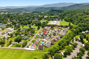 Aerial view of a peaceful residential neighborhood nestled in a lush valley, surrounded by rolling green hills and mountain vistas, with the property marked at the center of the community.
