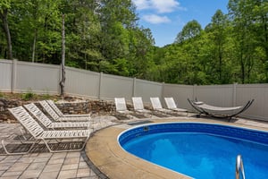 Surrounded by lush forested hills, the private pool area features sunny lounge chairs and a tranquil setting with natural stone walls and leafy privacy.