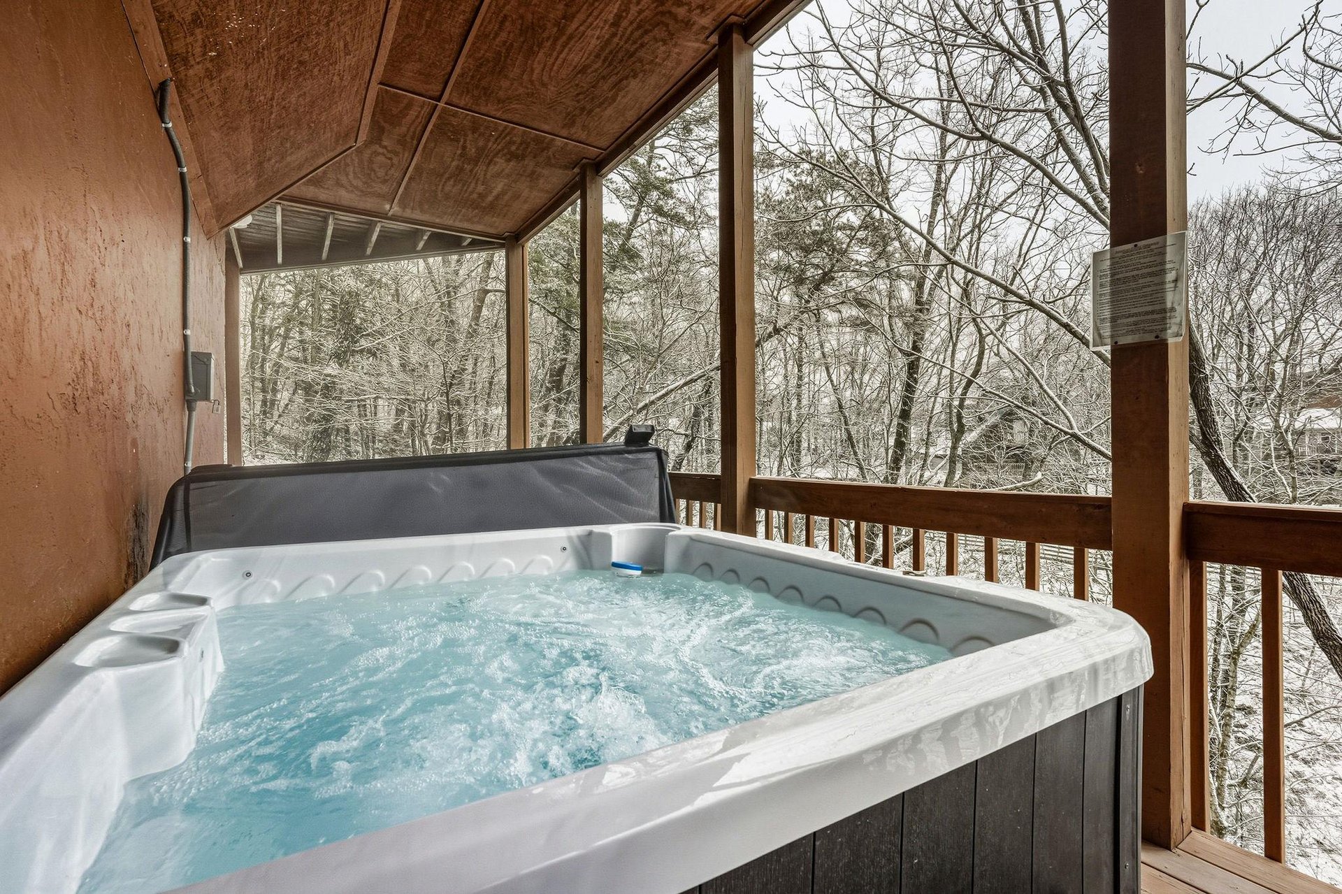 Soak in your private hot tub while winter trees create a peaceful backdrop on your covered deck.