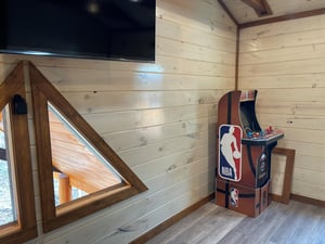 Unwind in this cozy loft game room featuring warm wood walls, an NBA arcade machine, and large TV for your entertainment.
