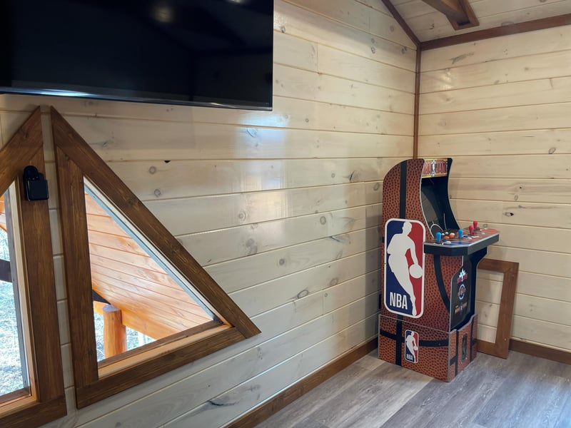 Unwind in this cozy loft game room featuring warm wood walls, an NBA arcade machine, and large TV for your entertainment.