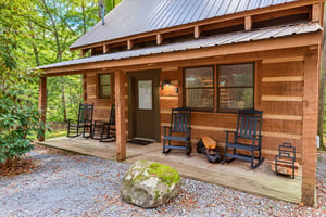 A charming wood cabin nestled in a peaceful forest setting, featuring a welcoming covered porch with classic rocking chairs for relaxing among the trees.