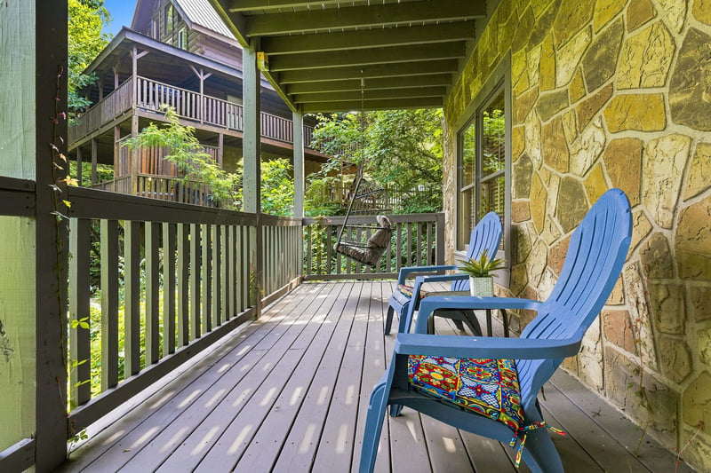 Settle into your private deck with a swing and cheerful blue chairs, surrounded by lush greenery and peaceful views of neighboring cabins tucked among the trees.