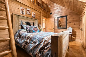 Drift off beneath the warm glow of woodpaneled walls and rustic charm. The handcrafted bed invites restful nights, while the lofted space above adds a cozy touch to your mountain retreat.