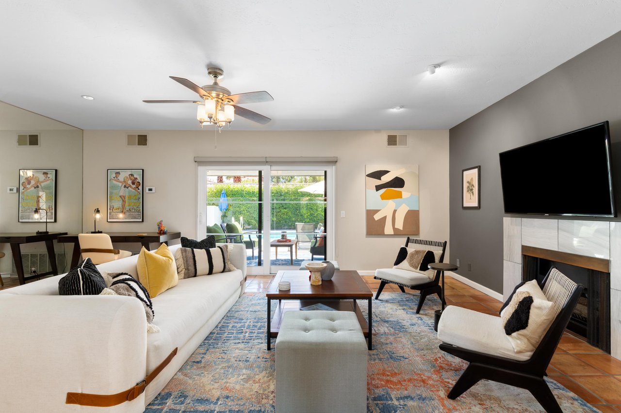 Spacious living room with flatscreen TV, fireplace, direct patio access, and pool views.