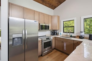 Your fully equipped kitchen invites you to prepare homecooked meals with stainless appliances, ample counter space, and natural light streaming through windows overlooking lush greenery.