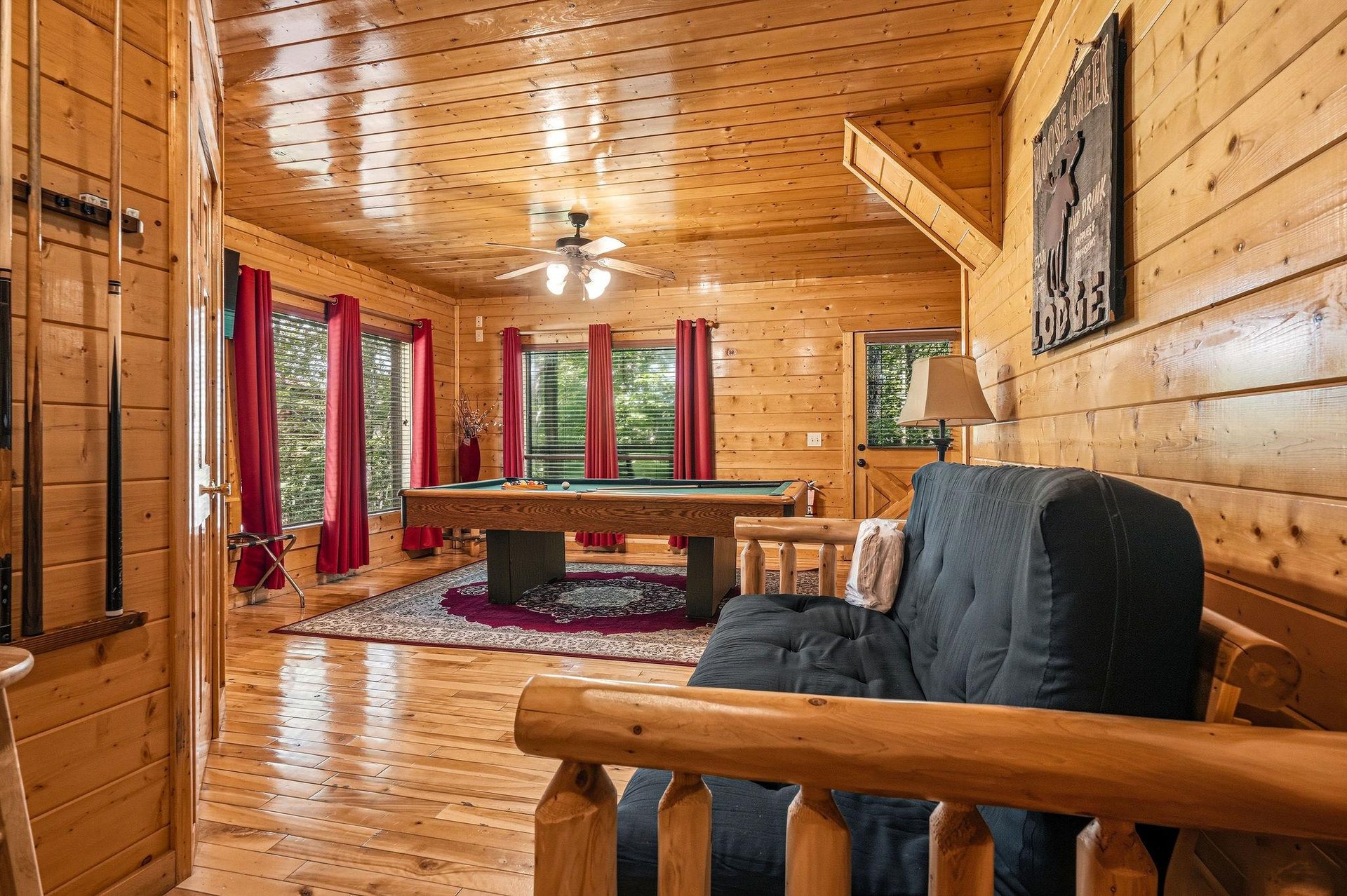 This inviting cabin living space features warm wood paneling, a pool table for friendly competition, and cozy seating where you can unwind after a day of adventure.