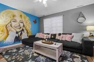 Relax in your stylish living room with plush seating, a bold mural, and touches of pink and gray that create a warm, welcoming atmosphere.