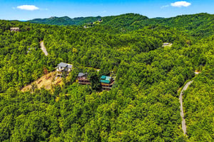 Aerial view of vacation rental cabins nestled within lush mountain forest, showcasing the propertys secluded hillside location and winding access roads through dense woodland.