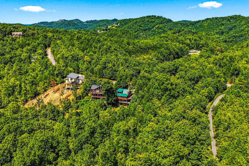 Aerial view of vacation rental cabins nestled within lush mountain forest, showcasing the propertys secluded hillside location and winding access roads through dense woodland.