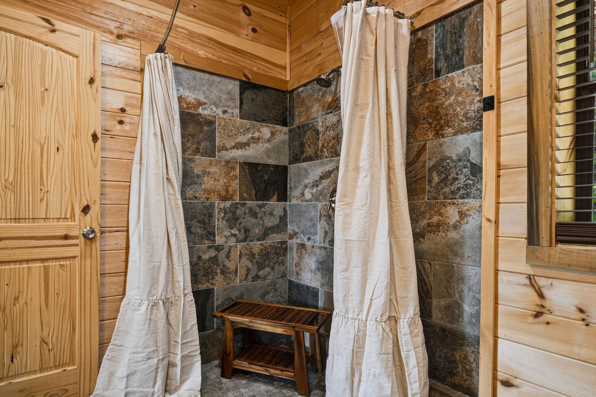 Step into your rustic retreat natural stone tile, warm wood walls, and soft linen curtains create a tranquil shower sanctuary.