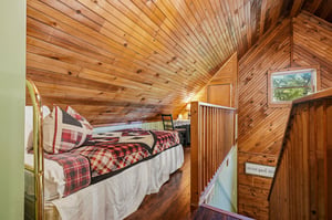Your cozy loft bedroom features warm wood ceilings and plaid bedding, creating the perfect rustic retreat under the eaves.