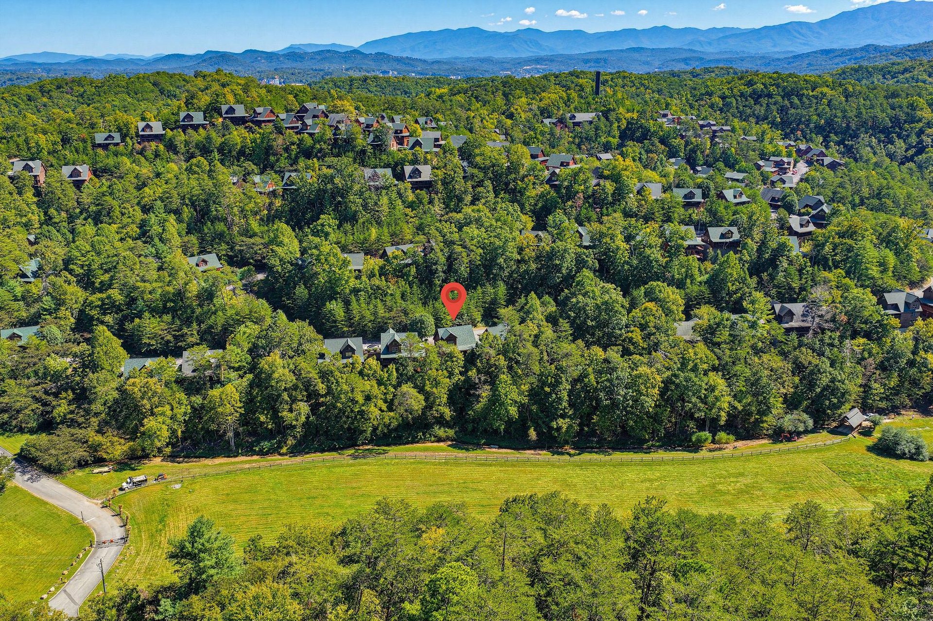 Aerial view of the property nestled in a lush, forested neighborhood with rolling hills and stunning mountain ranges stretching across the horizon.