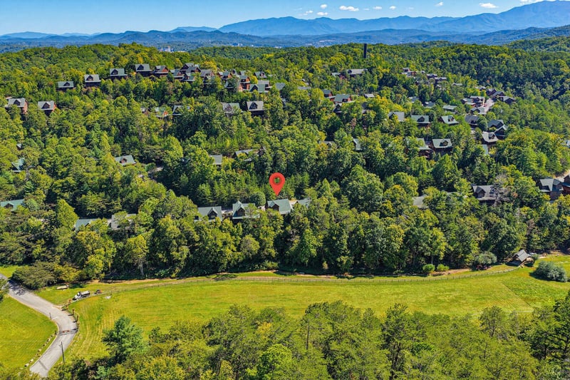 Aerial view of the property nestled in a lush, forested neighborhood with rolling hills and stunning mountain ranges stretching across the horizon.
