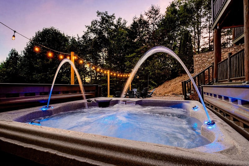 Soak under the stars in your private hot tub with water arcs and string lights creating a magical evening ambiance.