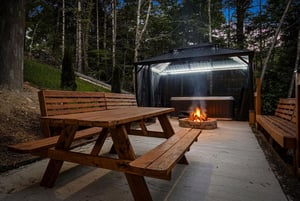 A private outdoor retreat nestled in the woods where you can unwind by the fire pit, soak in the sheltered hot tub, and enjoy peaceful evenings under the trees.