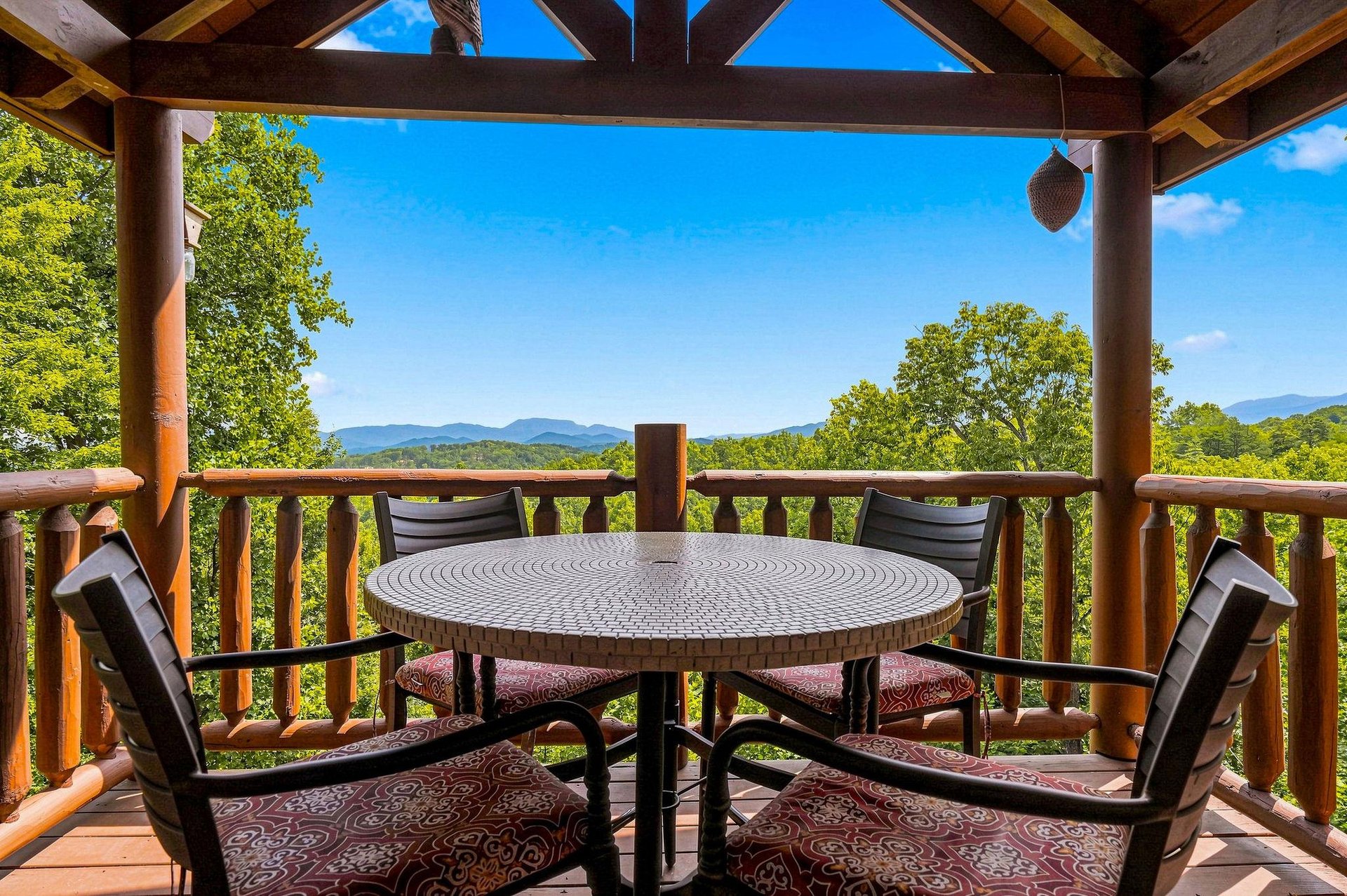 This covered deck features a peaceful mountain backdrop visible through lush forest surroundings. The circular table and cushioned seating create a welcoming outdoor dining or relaxation spot.