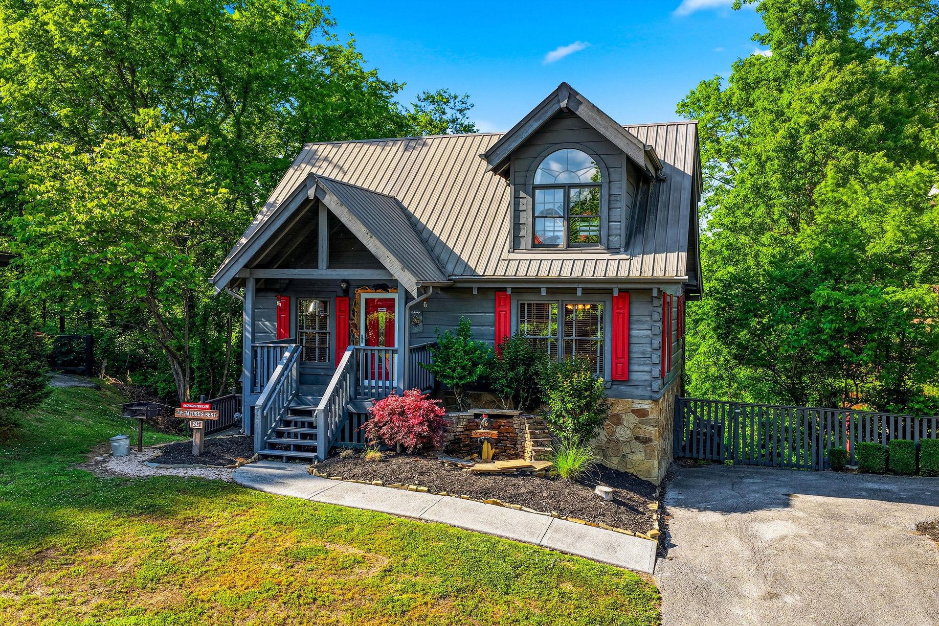 Charming mountain cabin with red shutters nestled among lush trees, featuring covered porch and landscaped grounds for a peaceful retreat.