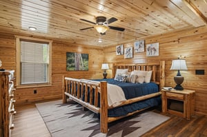 Sink into your cozy log bed beneath rustic wood walls and wildlife art, where a gentle ceiling fan keeps your retreat comfortable and welcoming.